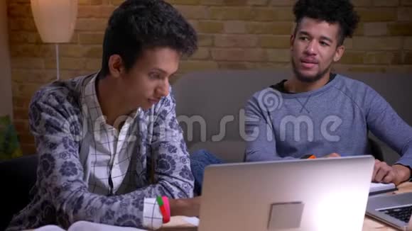 印度和非裔美国男学生使用笔记本电脑的特写镜头讨论一个大学项目视频的预览图