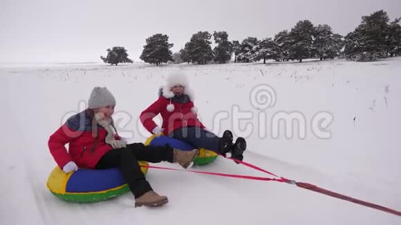 十几岁的女孩骑着雪碟在雪道上笑孩子们在冬天玩雪橇慢动作视频的预览图