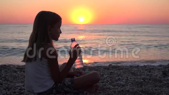 日落海滩上的儿童饮用水观看海浪的儿童海滨女孩视频的预览图