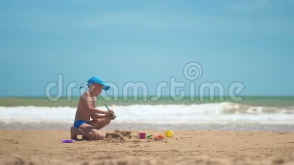 一个小男孩正在大海上的沙子里玩耍小腿和手指大海的背景是黄沙和碧水视频的预览图