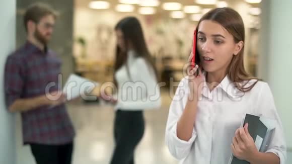 年轻女孩的肖像在工作场所用手机聊天背景是聊天的人慢慢视频的预览图