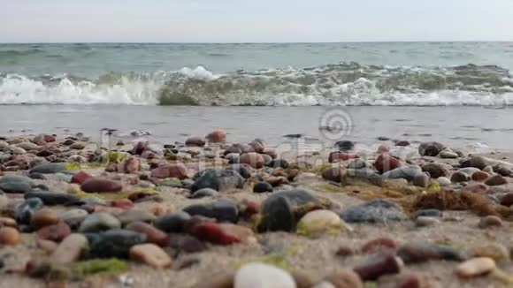 波浪拍打着海岸沙滩上有鹅卵石低点射击模糊的前景中五颜六色的鹅卵石视频的预览图