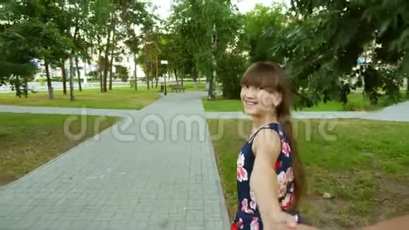 女孩在温暖的夏日傍晚牵着男人微笑着快乐的女人穿过公园大笑视频的预览图