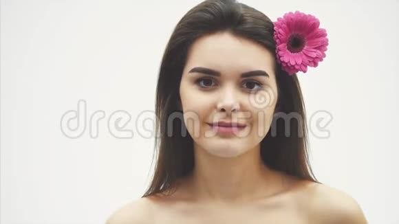 美丽的年轻美丽的女孩被孤立在白色的背景上头发上有一朵粉红色的花情感化妆品视频的预览图