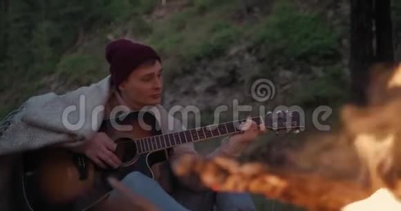 一个年轻人坐在河岸上的火堆前弹吉他视频的预览图
