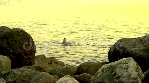 日落时分一位年轻女子在海中的岩石中游泳视频的预览图