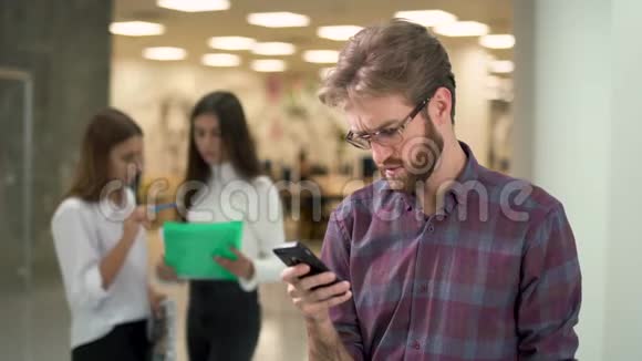 一个严肃的年轻人站在一个中心专注于写短信一个拿着文件的员工走近了他视频的预览图