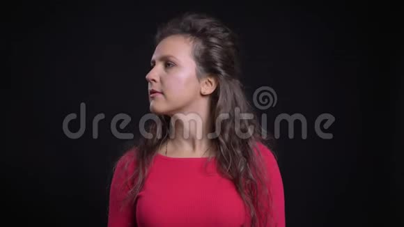 白种人女人的红色肖像转过头平静地注视着黑色背景的镜头视频的预览图