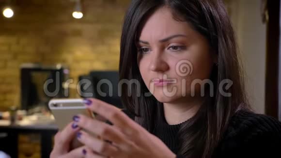 一位成年白种人深色头发的女商人坐在笔记本电脑前随意浏览电话的特写照片视频的预览图