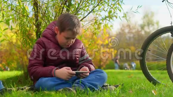 坐在草地上玩智能手机的青少年妈妈坐下了视频的预览图