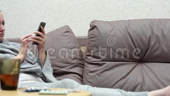 一个女人家里感冒了躺在沙发上用电话视频的预览图