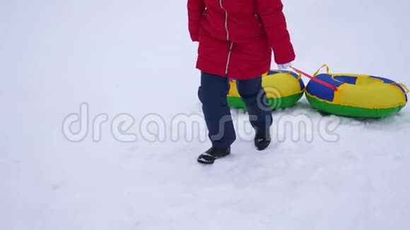 女孩抱着雪碟爬上高高的雪山孩子们在冬天玩雪橇山区度假胜地圣诞节视频的预览图