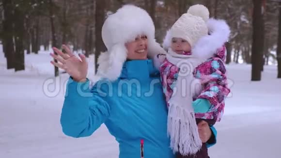妈妈抱着她的小女儿在冬天下雪公园笑着挥手圣诞周末妈妈带着孩子散步视频的预览图