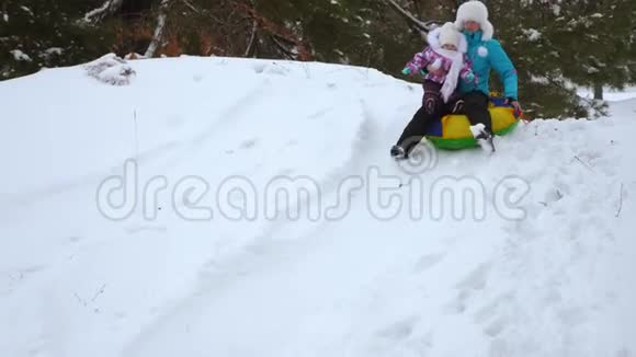 妈妈和她的小女儿从公园的雪山上滚出雪橇笑了起来视频的预览图