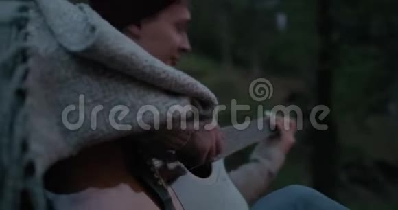 一个年轻人坐在河岸上的火堆前弹吉他视频的预览图