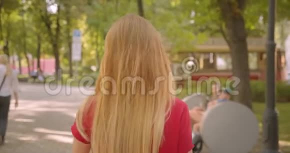 特写后景照片年轻的金发长毛可爱的女性走在公园里转身看着相机视频的预览图