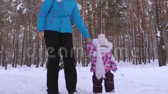 小女孩和她的母亲在公园里的雪冬路上牵手散步圣诞节视频的预览图