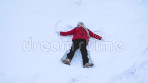 少女使雪天使挥舞着她的手臂和腿躺在雪上视频的预览图