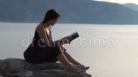 一个年轻的女孩正在海边的一个美丽的地方读一本书动作缓慢视频的预览图