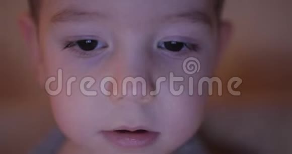 一个快乐的孩子的夜晚照片他的脸看着一台平板电脑眼睛里有淡淡的反射视频的预览图