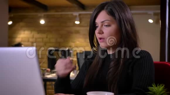 一张成年白人黑发女商人在办公室使用笔记本电脑咳嗽的特写照片视频的预览图