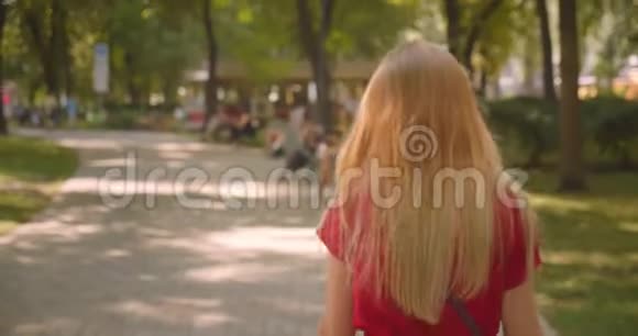 特写后景照片年轻的金发长毛可爱的女性走在公园里转身看着镜头视频的预览图