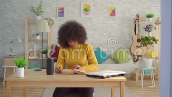 一个留着非洲发型的黑人妇女喜欢语音助手在桌边看书视频的预览图