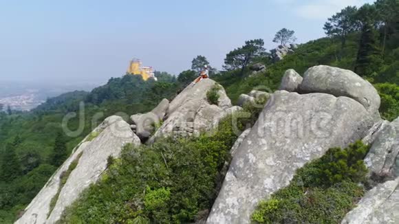 坐在山上岩石上的鸟瞰女孩视频的预览图