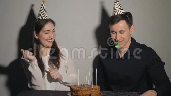 漂亮的女孩和男人庆祝一个节日坐在一张桌子上拿着蛋糕和蜡烛玩聚会吹箫视频的预览图