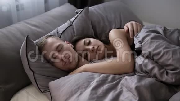 白种人年轻夫妇在灰色床单上睡在家里的床上的肖像上午时间视频的预览图