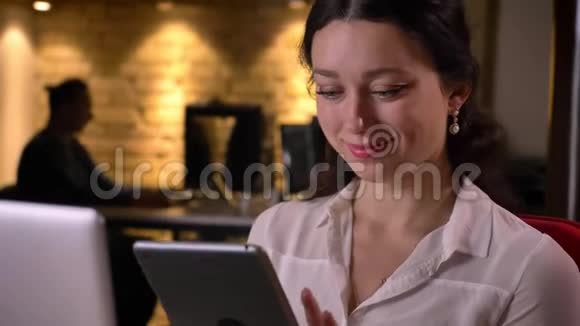 年轻白种女性上班族使用平板电脑在室内工作场所获得惊喜和微笑的特写镜头视频的预览图