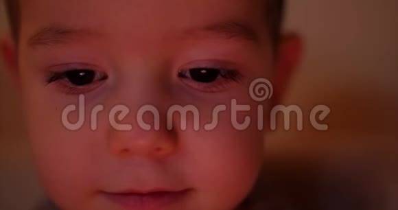 一个快乐的孩子的夜晚照片他的脸看着一台平板电脑眼睛里有淡淡的反射视频的预览图