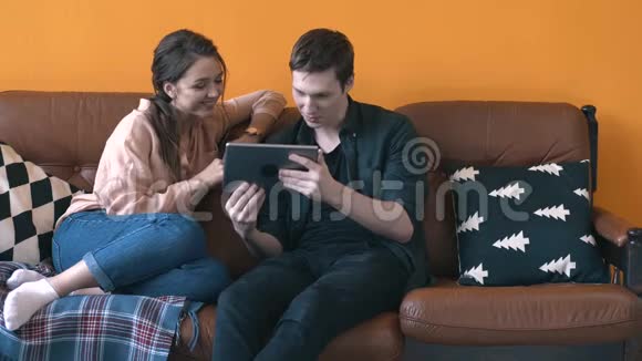 一对幸福的年轻夫妇坐在家里的沙发上观看平板电脑屏幕库存录像人与人视频的预览图