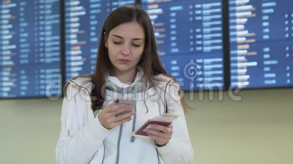 手里拿着护照和机票的漂亮女孩用电话核对信息板上的出发时间视频的预览图