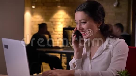 年轻开朗的女性办公室的特写镜头随意地在电话上交谈微笑着在笔记本电脑上打字视频的预览图