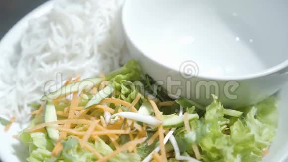 盘子上的空碗靠近面条胡萝卜黄瓜和生菜的维生素沙拉厨师准备食物视频的预览图