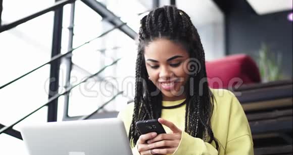 一位有魅力的非洲年轻女士坐在楼梯上然后在她的智能手机上打字的肖像视频的预览图