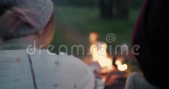 一对年轻夫妇坐在河边的森林里聊天煎棉花糖视频的预览图