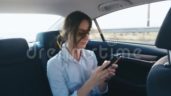 描绘年轻女性在与司机一起乘汽车旅行时使用智能手机的肖像女孩在查邮件聊天视频的预览图