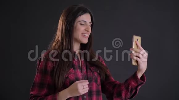 年轻漂亮的白种人长发女孩用黑色智能手机在电视上聊天的肖像视频的预览图