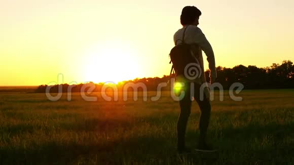 一个女孩在日落时走在绿色的田野上视频的预览图