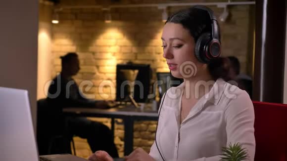 笔记本电脑前戴耳机听音乐的年轻漂亮女办公室职员的特写镜头视频的预览图