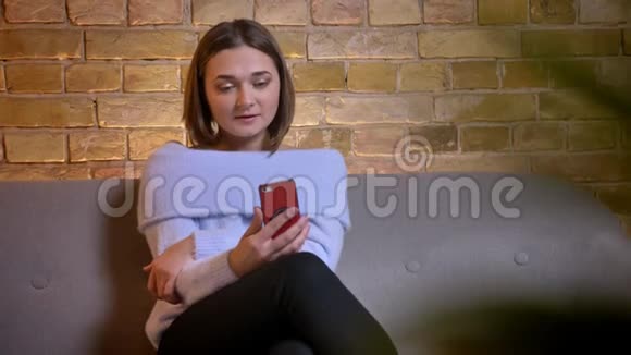 在舒适的家中坐在沙发上的年轻美丽的白种人女性通过视频电话聊天的特写镜头视频的预览图
