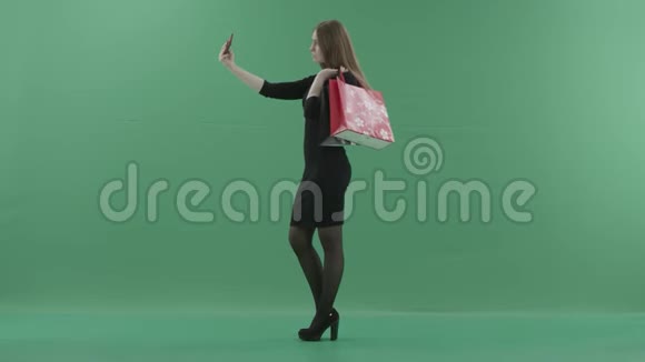 穿着黑色小裙子的漂亮女人拿着购物袋在手机上自拍她是视频的预览图