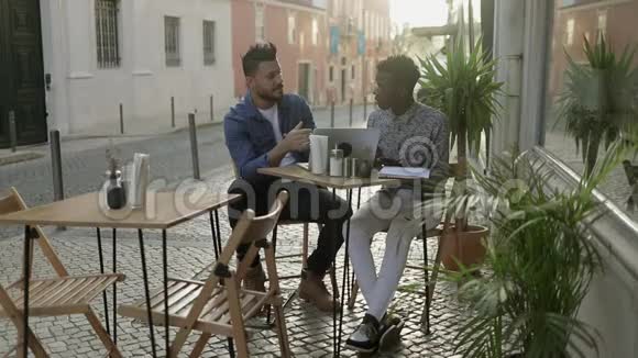 多种族男子与数字设备交谈户外咖啡馆视频的预览图