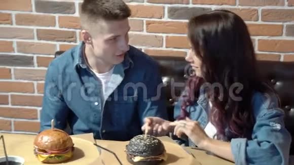快乐的一对夫妇在咖啡馆里一起吃汉堡和玩视频的预览图