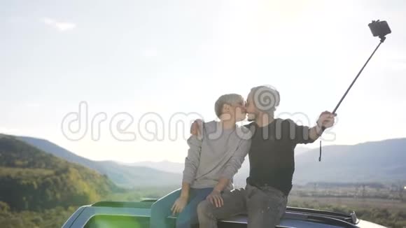 幸福的一对夫妇坐在车顶上在山上拥有智能手机摄像头视频的预览图