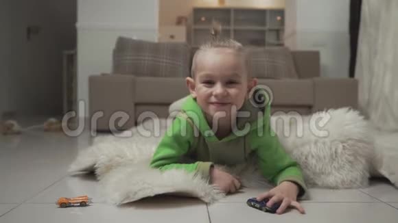 小男孩的肖像时尚的发型玩玩具车躺在地板上毛茸茸的地毯视频的预览图