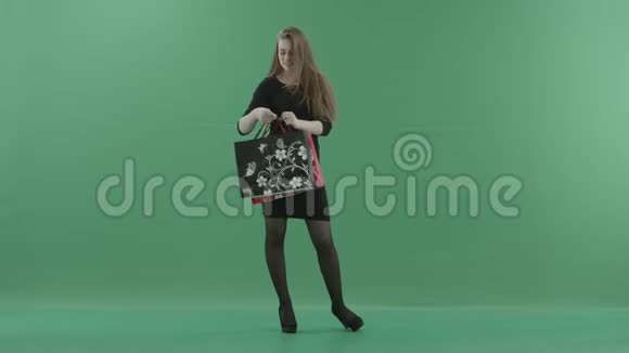 美丽快乐的女人穿着黑色的小裙子摆姿势用购物袋旋转她站在工作室里视频的预览图