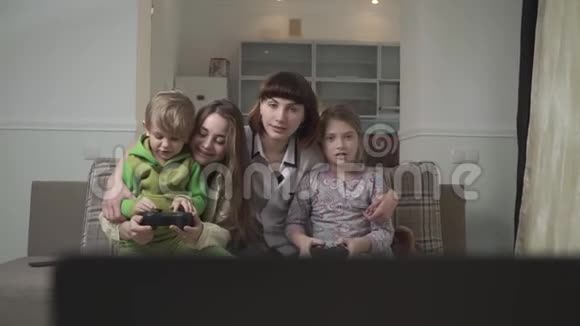 幸福一家四口玩电子游戏两个小孩子拿着操纵杆有趣的家庭假日视频的预览图